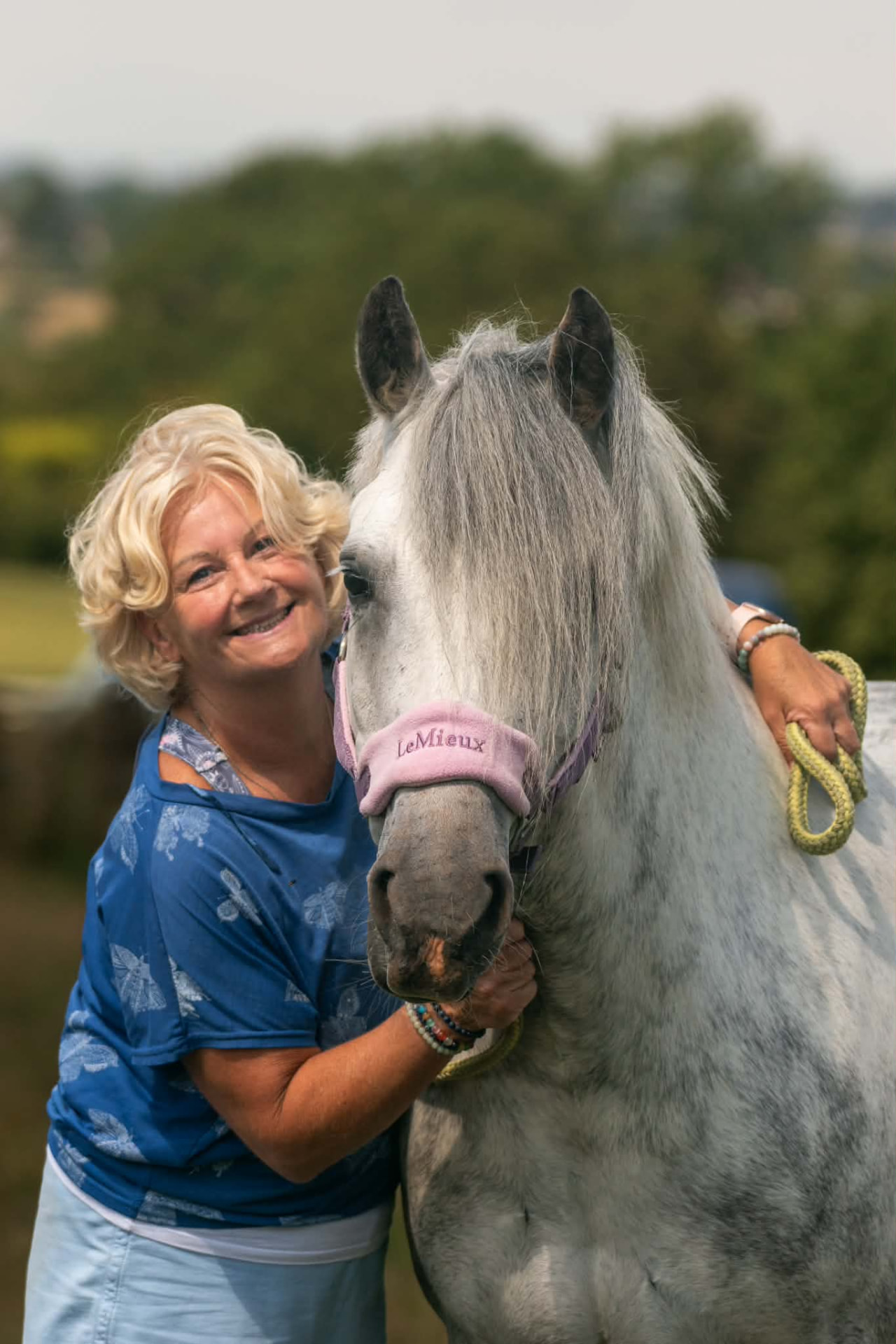 Smiling woman hugging her white Welsh pony