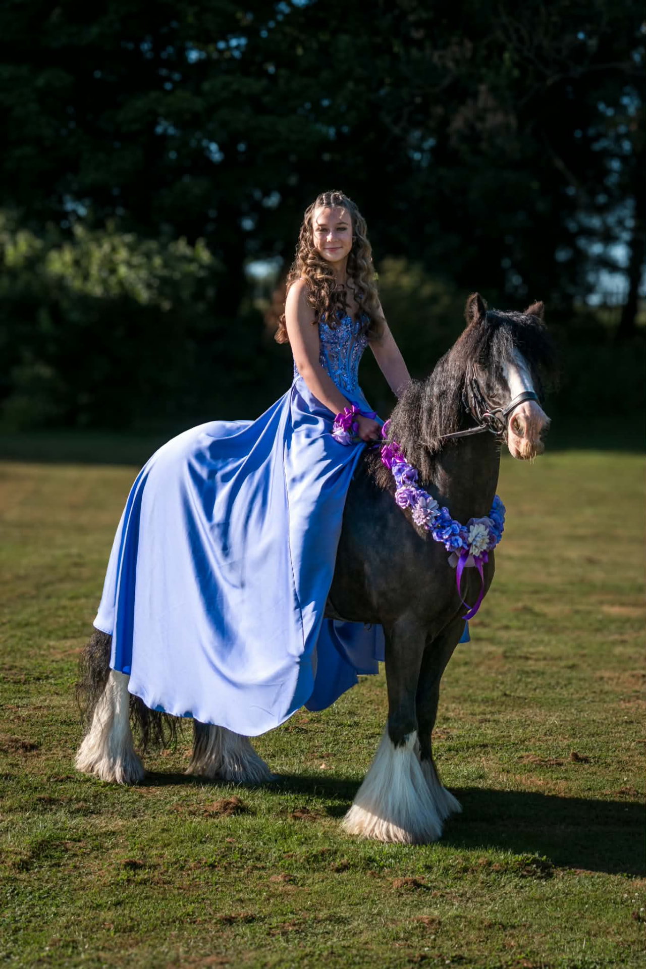 Girl in a blue prom dress with a flower garland, riding a black and white cob