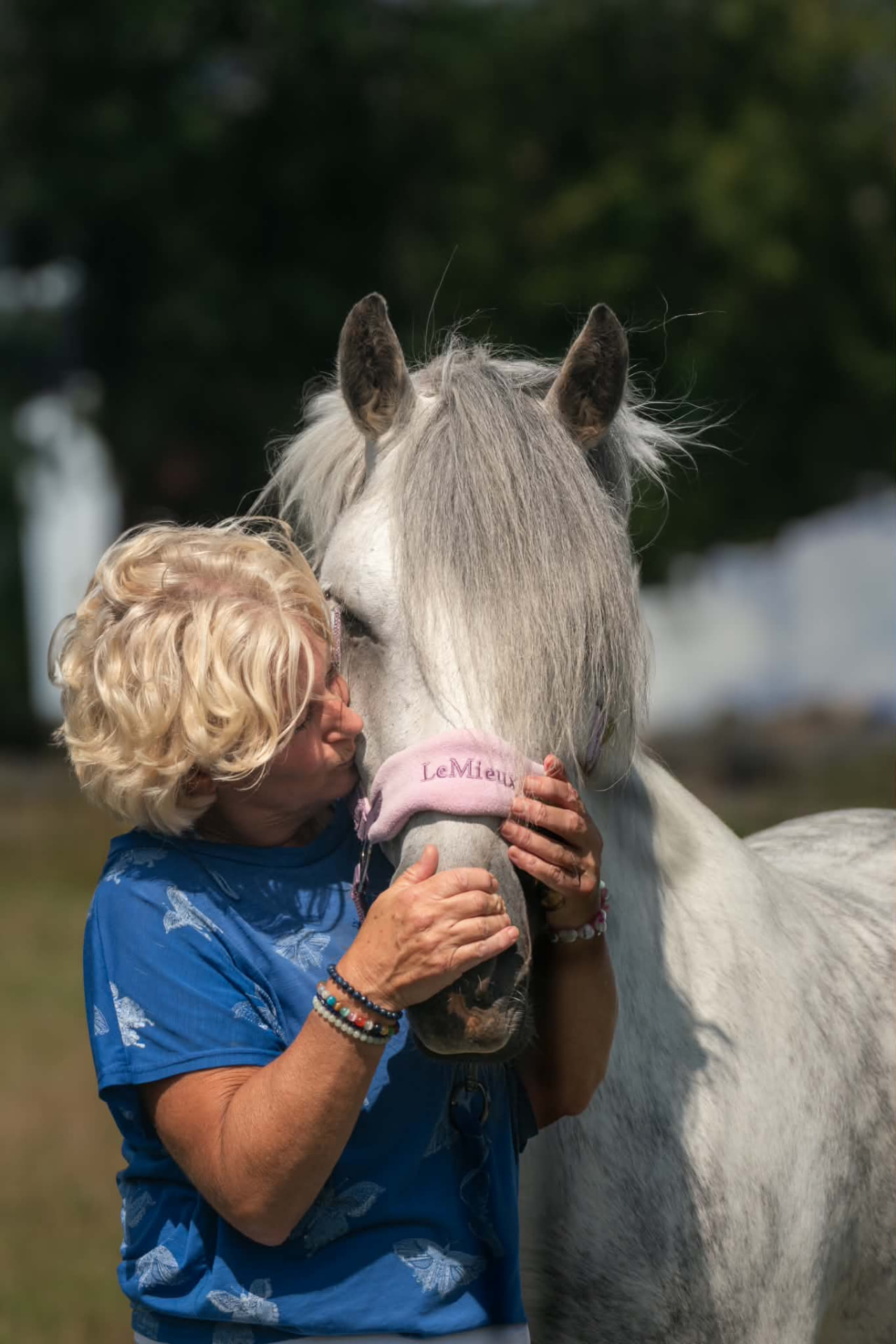 Woman in a butterfly-print top kissing her white pony’s nose