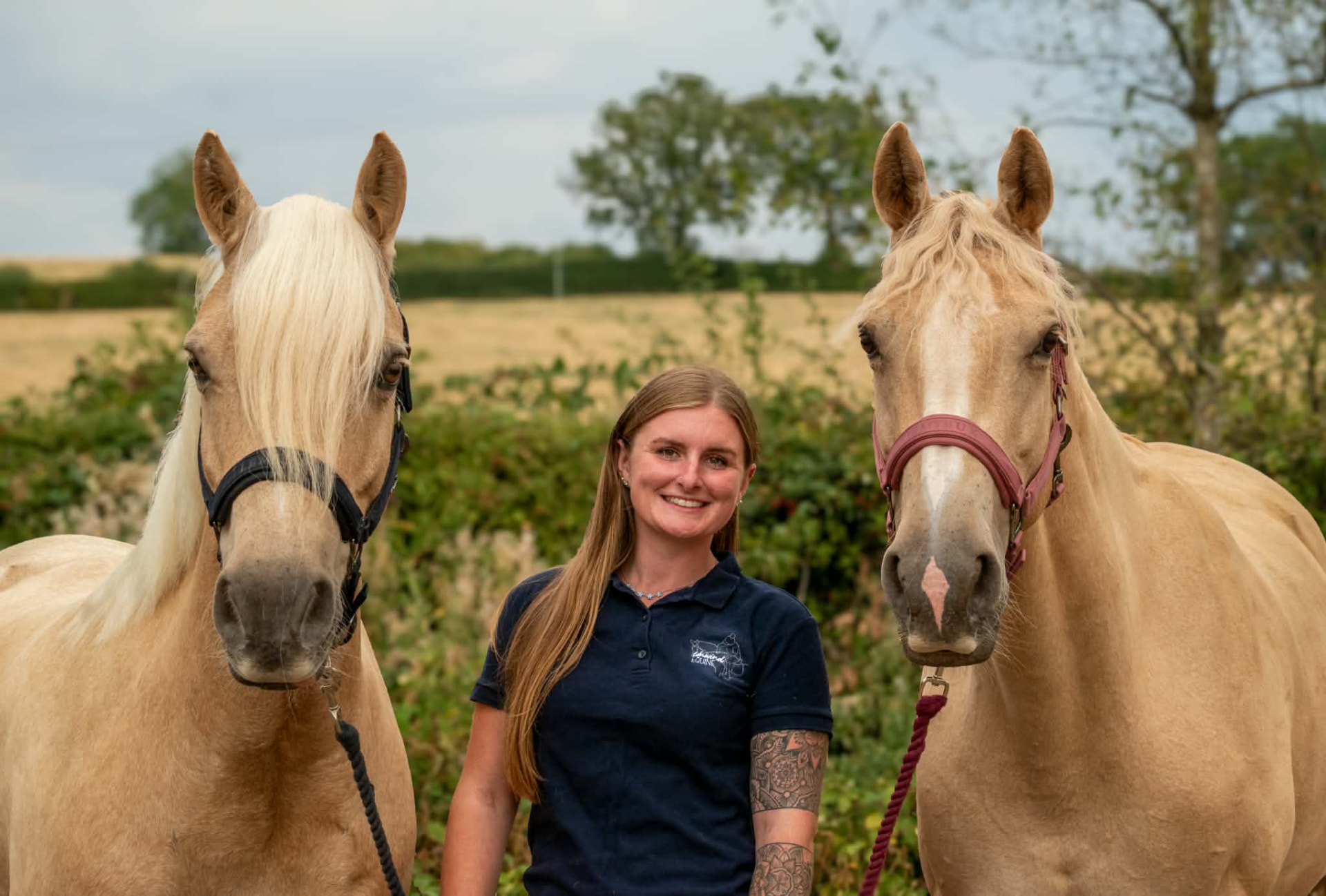 Jess standing between her two palomino horses in a paddock