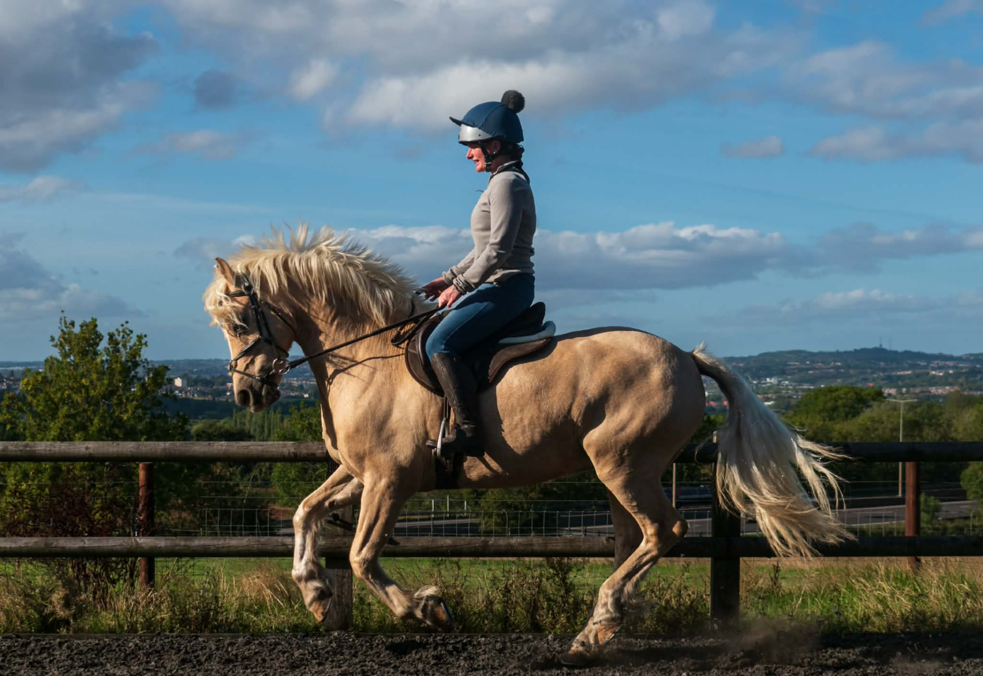 Rider smiling as her palomino pony trots past a wooden fence